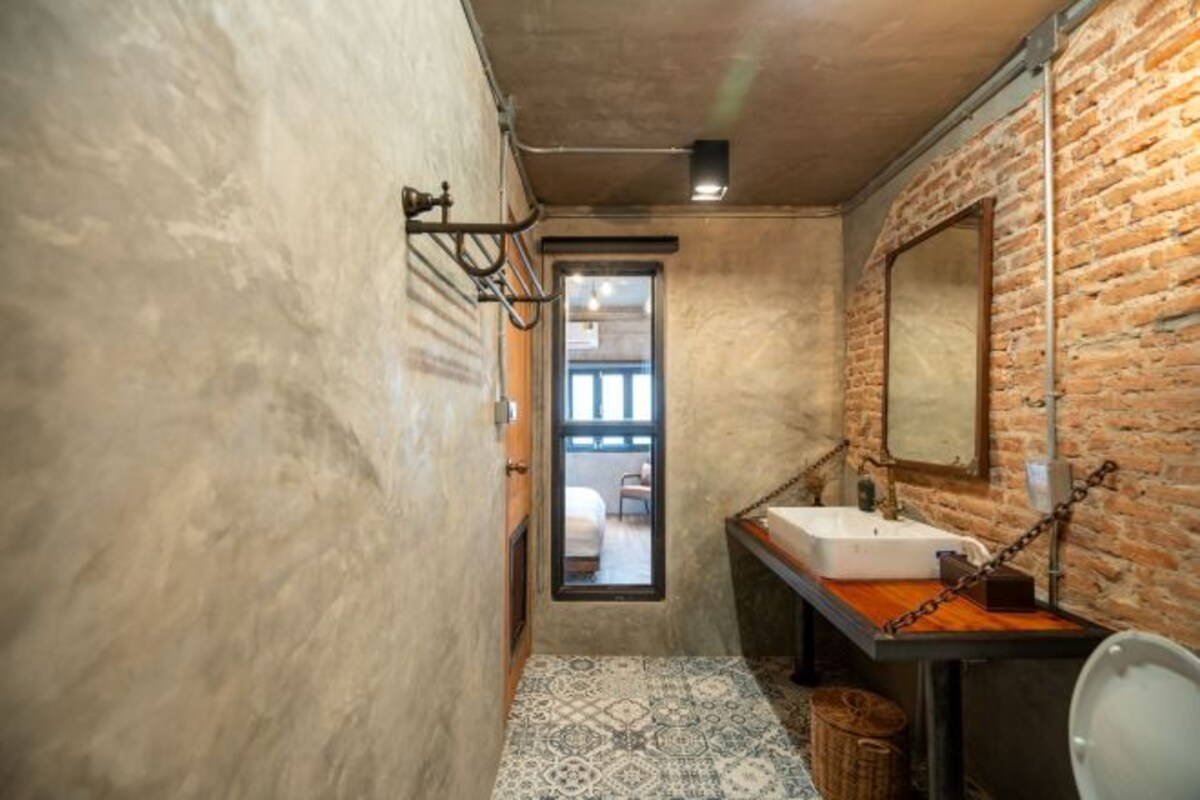 A narrow bathroom with a rustic brick wall, a white sink, and a patterned floor.