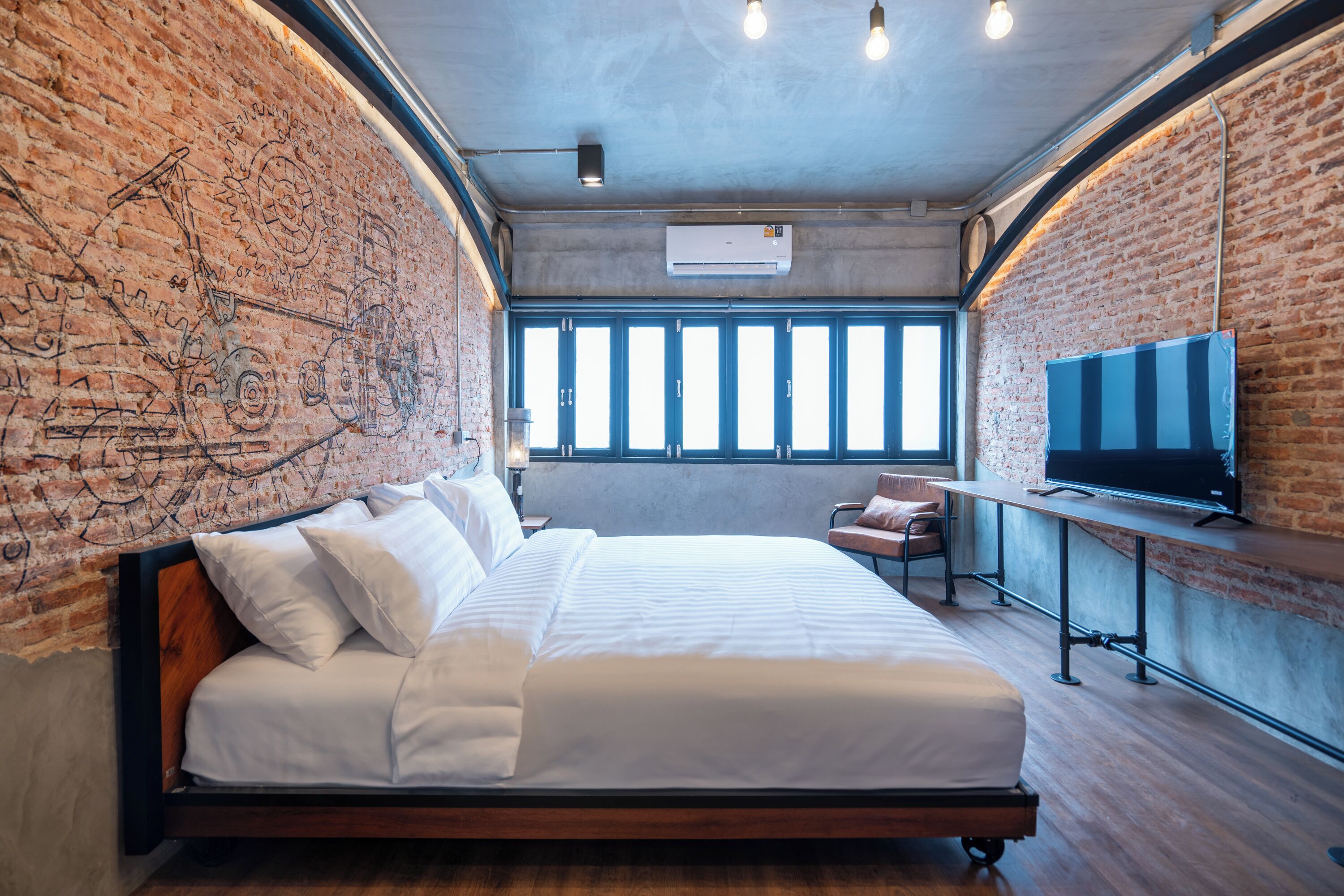 Una habitación de hotel moderna con pared de ladrillo, una cama grande, un televisor y un escritorio.