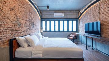 Una habitación de hotel moderna con pared de ladrillo, una cama grande, un televisor y un escritorio.