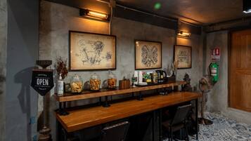 Zona de bar con mostrador de madera, dos planos técnicos enmarcados, un extintor y un letrero que indica aperitivos gratuitos.