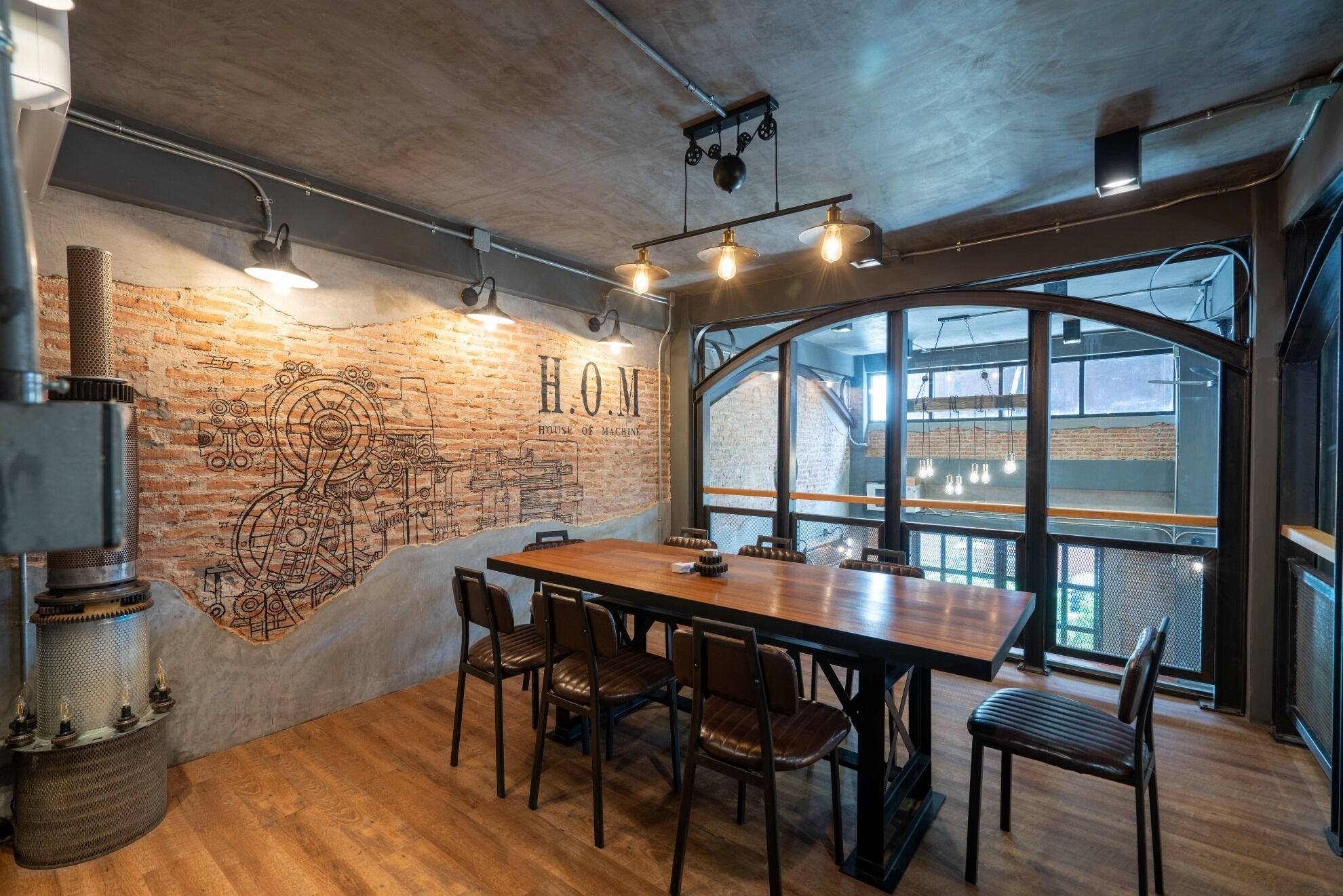 A modern dining area with a large wooden table and leather chairs, a brick wall with industrial design elements, and large windows offering views of the city.