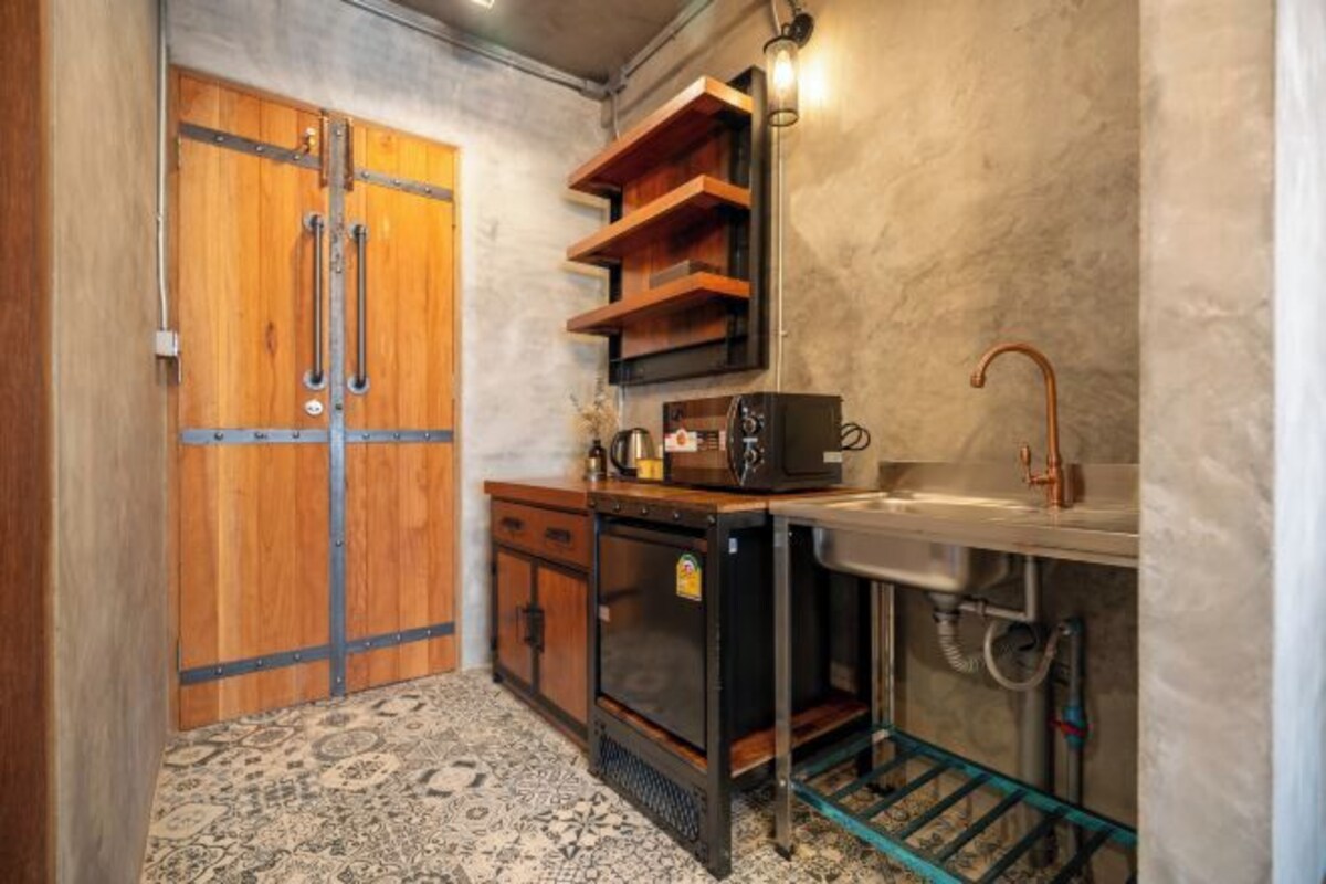 A compact kitchen with a wooden door, a built-in oven, a sink with a copper faucet, and a patterned floor.
