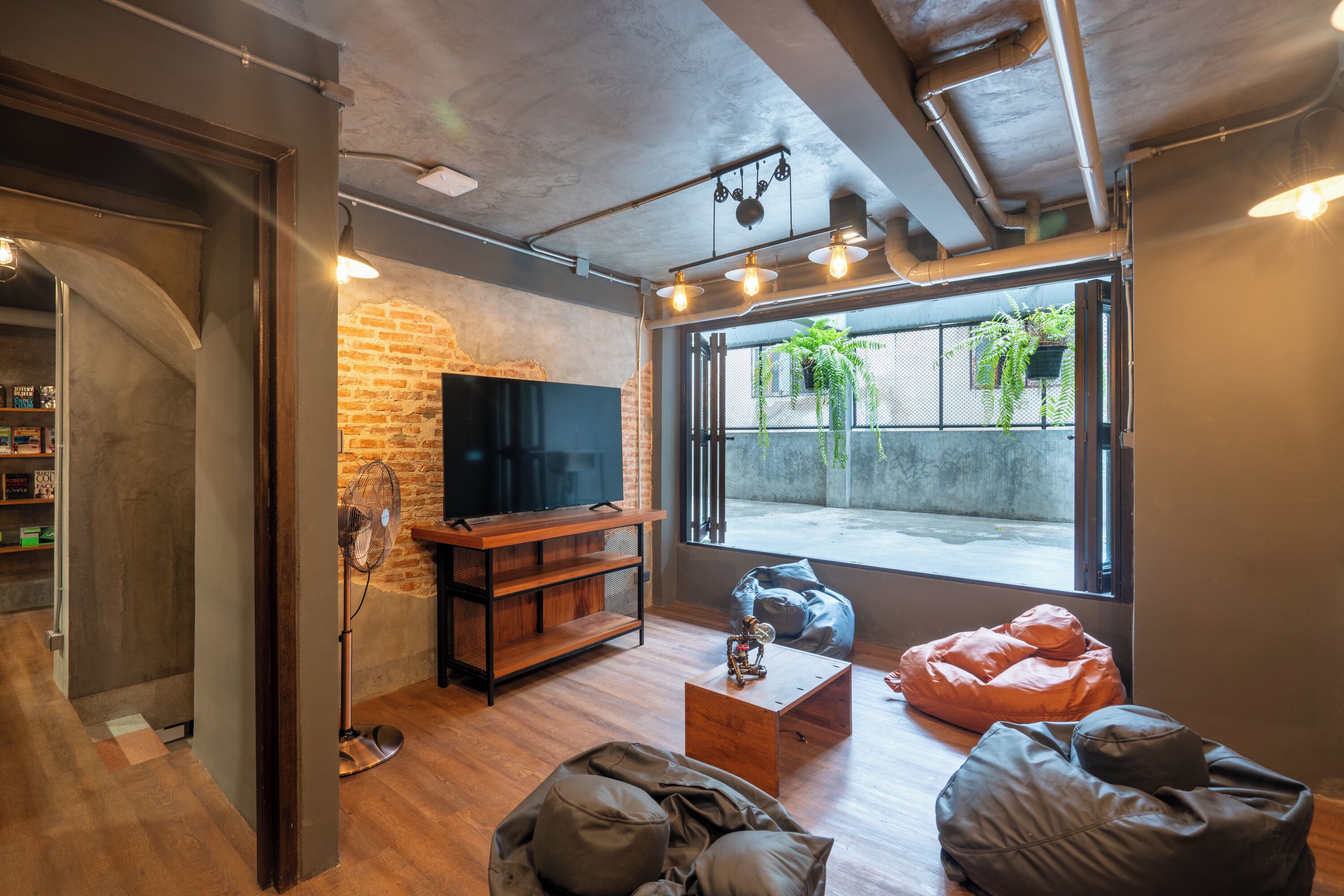 A modern living room with a brick wall, wooden flooring, a flat-screen TV, and large windows with a view of the outside.