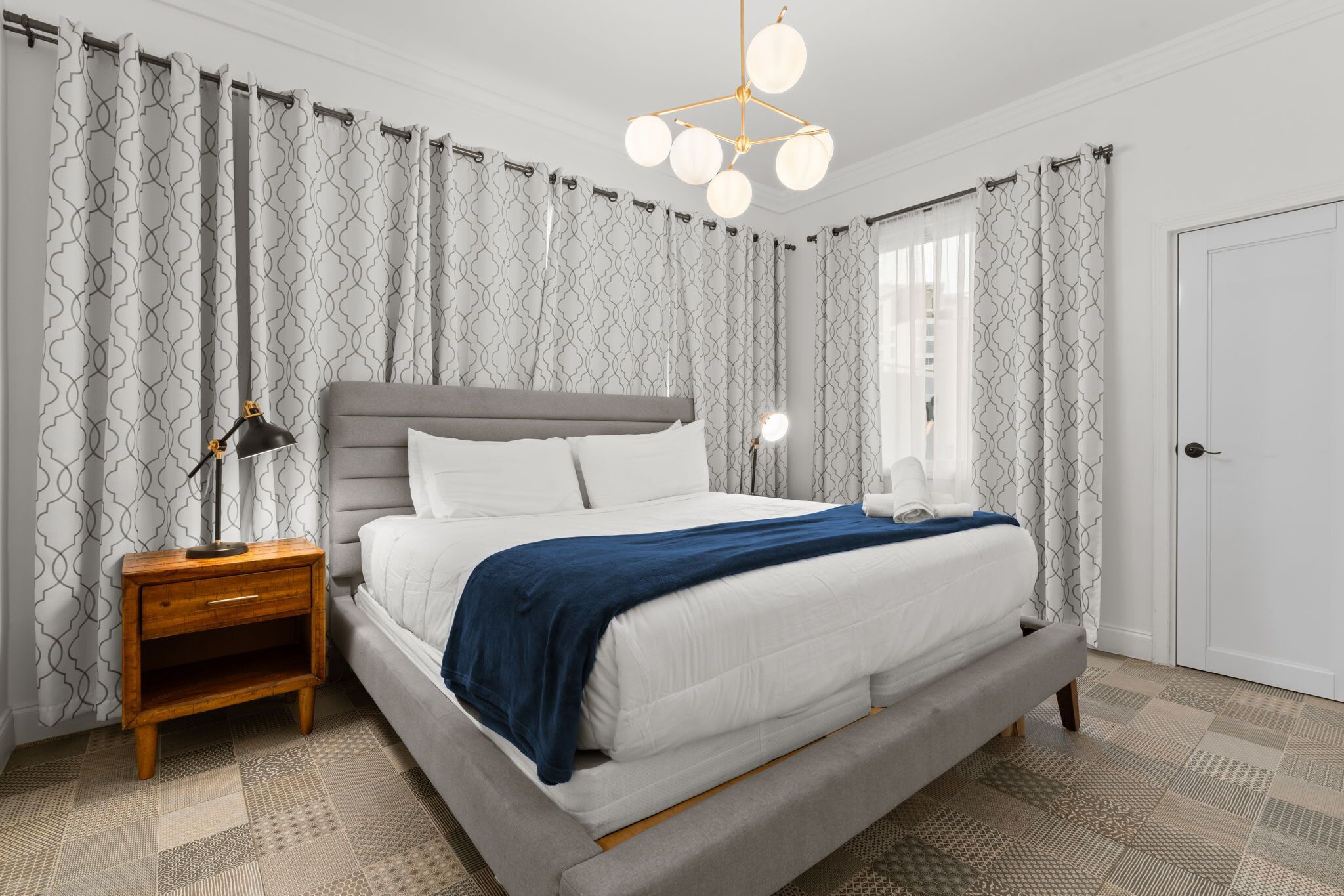 Un dormitorio con una cama grande, una mesita de noche, una lámpara y cortinas con estampado.