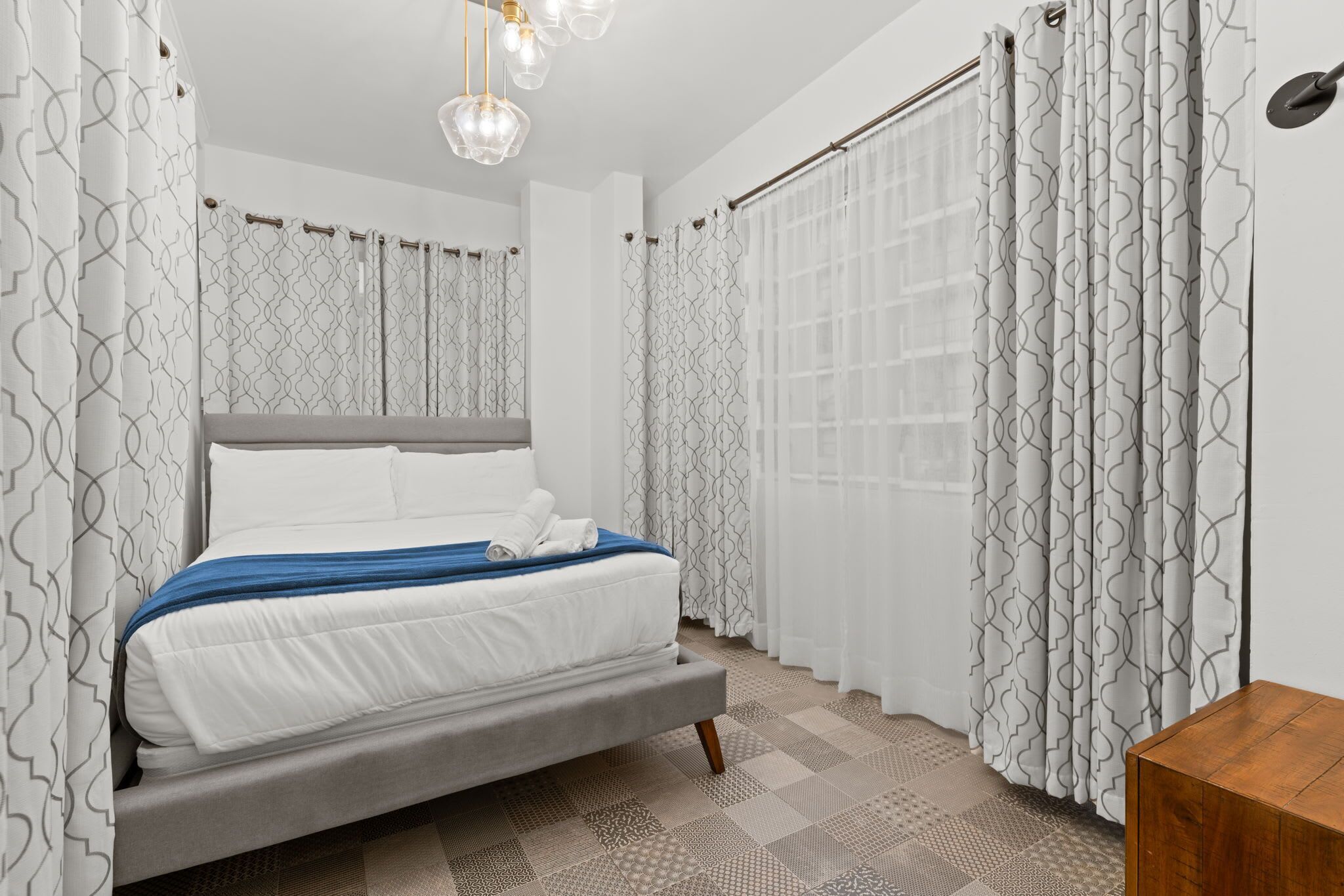 A bedroom with a bed, curtains, and a wooden nightstand.