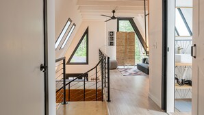 Un interior moderno con una escalera que conduce a una zona superior, un ventilador de techo y vistas al exterior.
