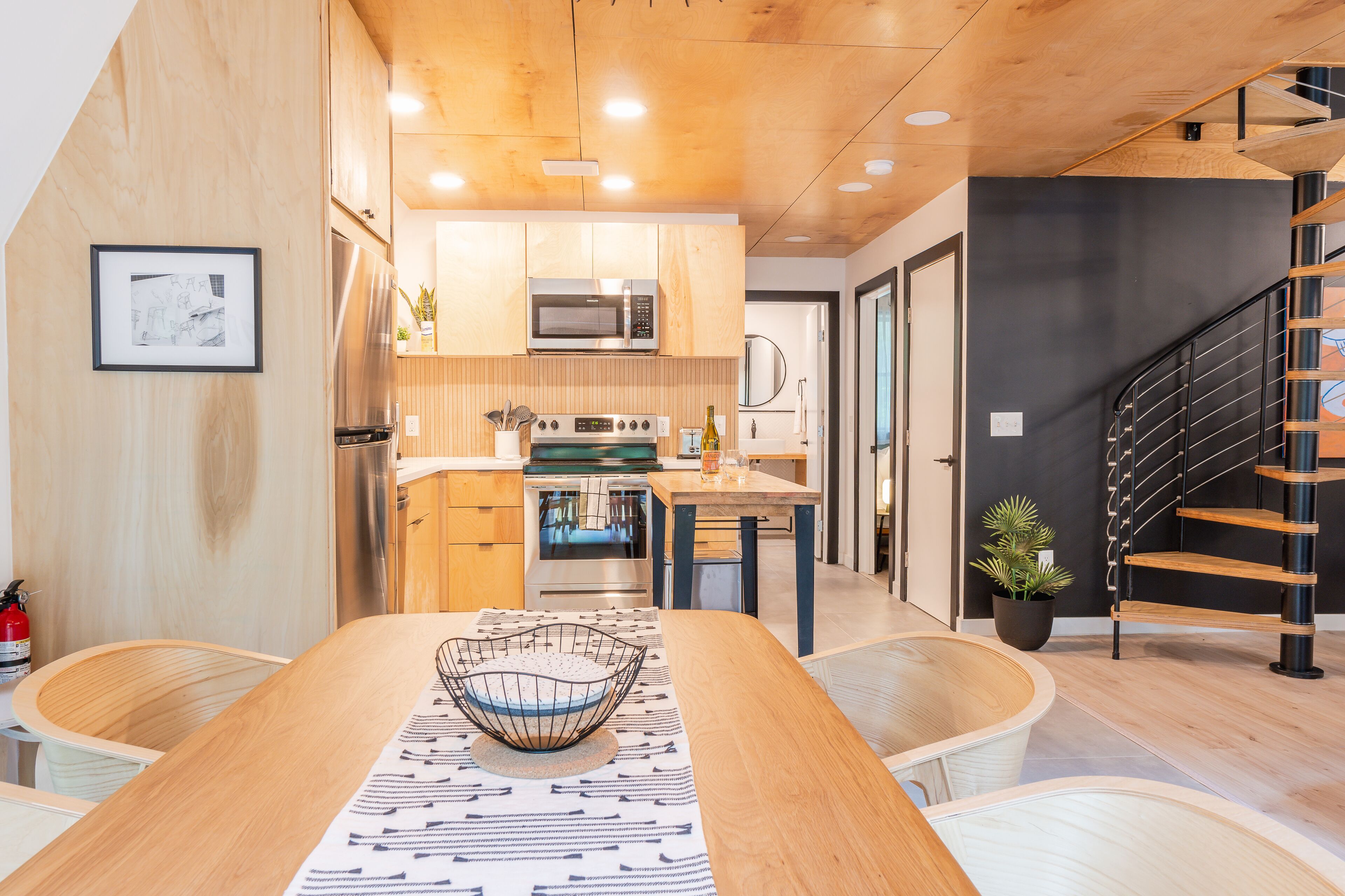 Een moderne keuken met houten kastjes, een roestvrijstalen koelkast, een magnetron, en een eethoek met een houten tafel en stoelen.