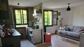 Cuina compacta amb fogó, rentapelats i batedora, a prop d'una zona d'estar amb sofà i taula petita.