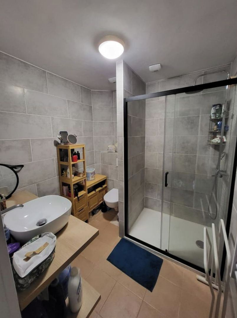 A modern bathroom with a glass shower enclosure, a white sink, and a wooden vanity.