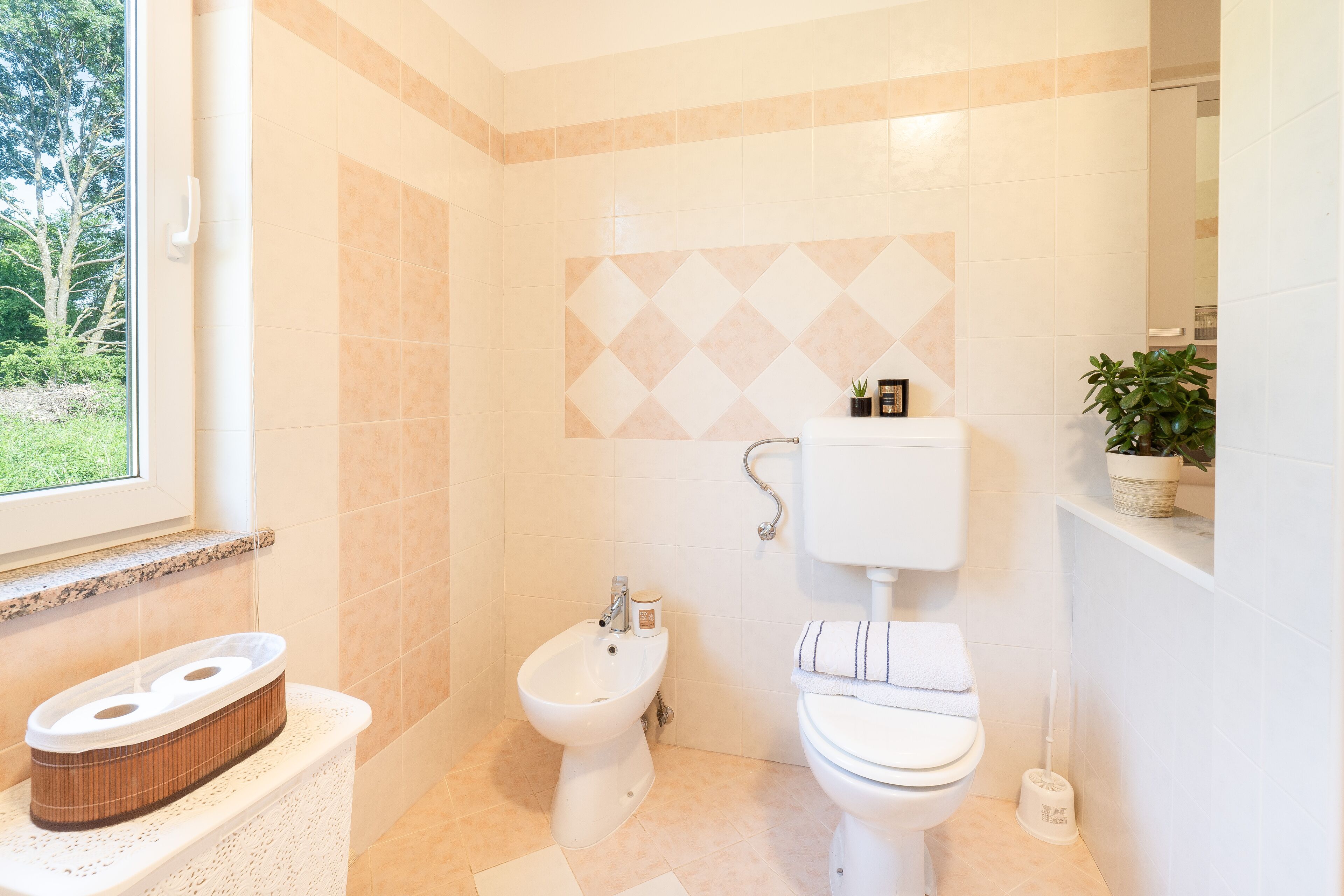 Ein Badezimmer mit Bidet, Toilette und einem Fenster mit Blick auf Grünflächen.