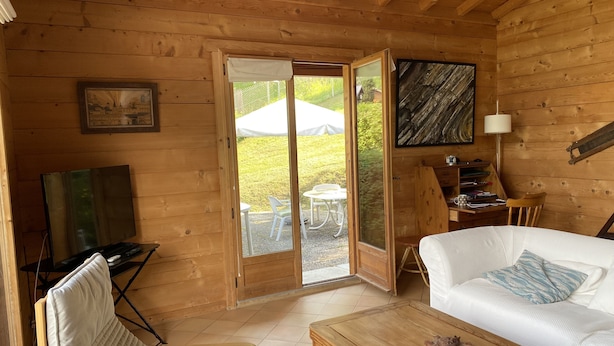 Ein gemütliches Blockhaus-Interieur mit Holzausstattung, einem weißen Sofa, einem Holztisch, einem gesteppten Sessel, einem Schreibtisch mit Computer und einem gerahmten Bild an der Wand.