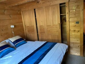 A wooden room with a bed, a wardrobe, and a small shelf with a key.