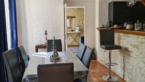 Een eetgedeelte met een tafel en stoelen, een bar met krukjes, en een keuken zichtbaar door een open doorgang.