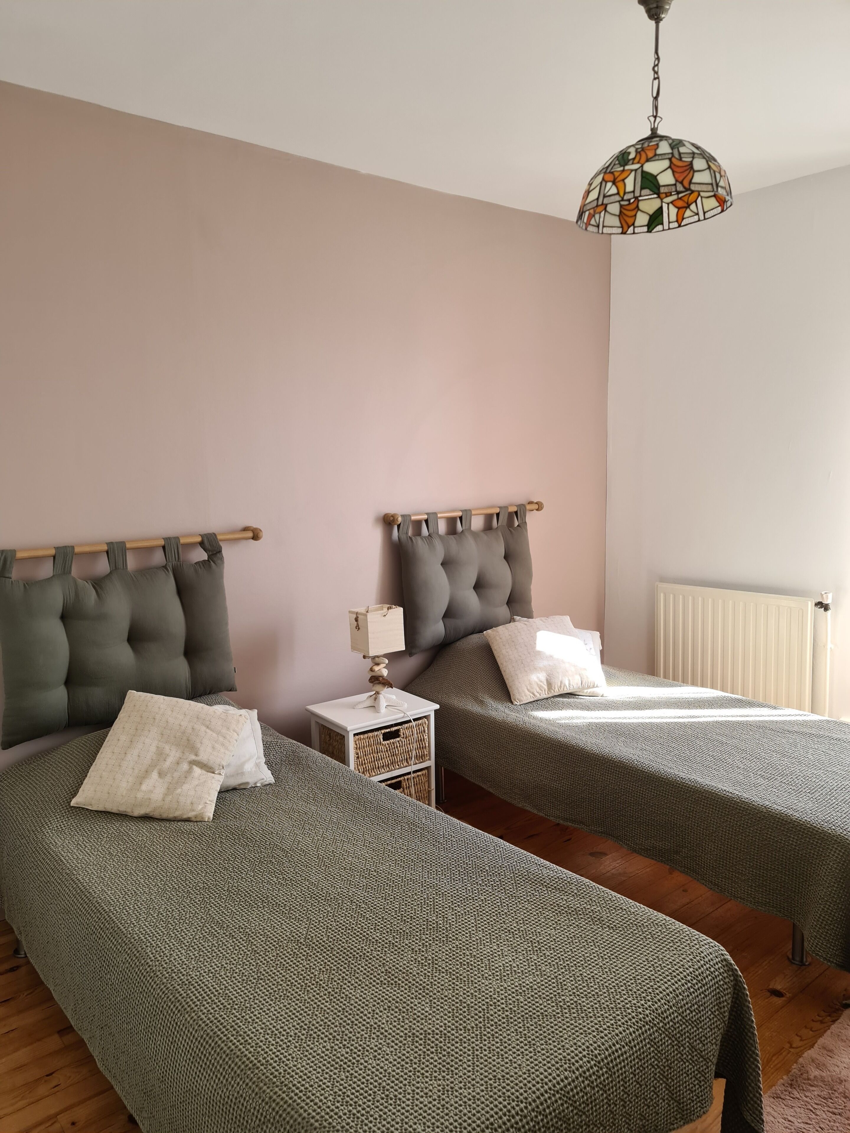 Quarto com duas camas, mesa de cabeceira com abajur e luminária pendente.