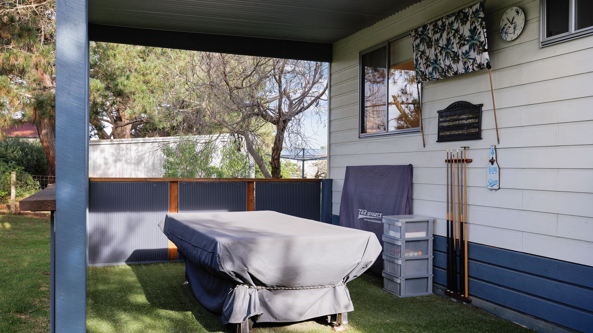 A covered outdoor area with a pool table, a covered seating area, and a clock on the wall.