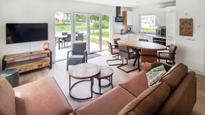 A modern living room with a large TV, a wooden bench, a sofa, and a dining area with a table and chairs. - Gorgeous home in Den Oever with WiFi (Den Oever)