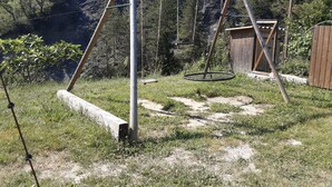 A wooden swing set in a grassy backyard with a wooden shed and a fence in the background. - Joli Pavillon Individuel et Privatif (Rigaud)