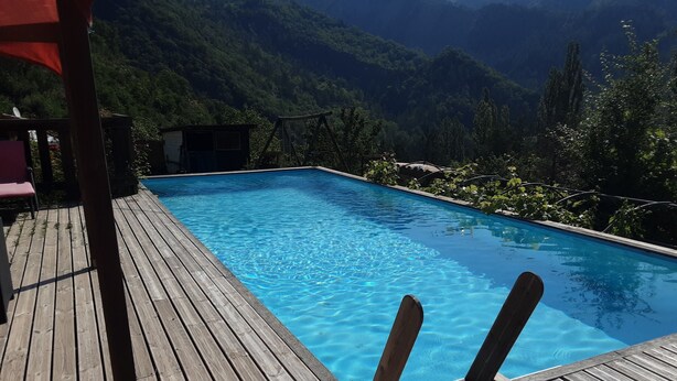 A wooden deck with a swimming pool, surrounded by lush greenery and mountains. - Joli Pavillon Individuel et Privatif (Rigaud)