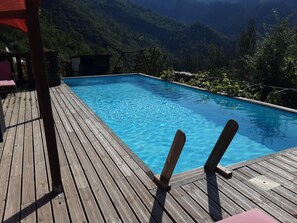 Une terrasse en bois avec une piscine, entourée d’une végétation luxuriante et de montagnes.