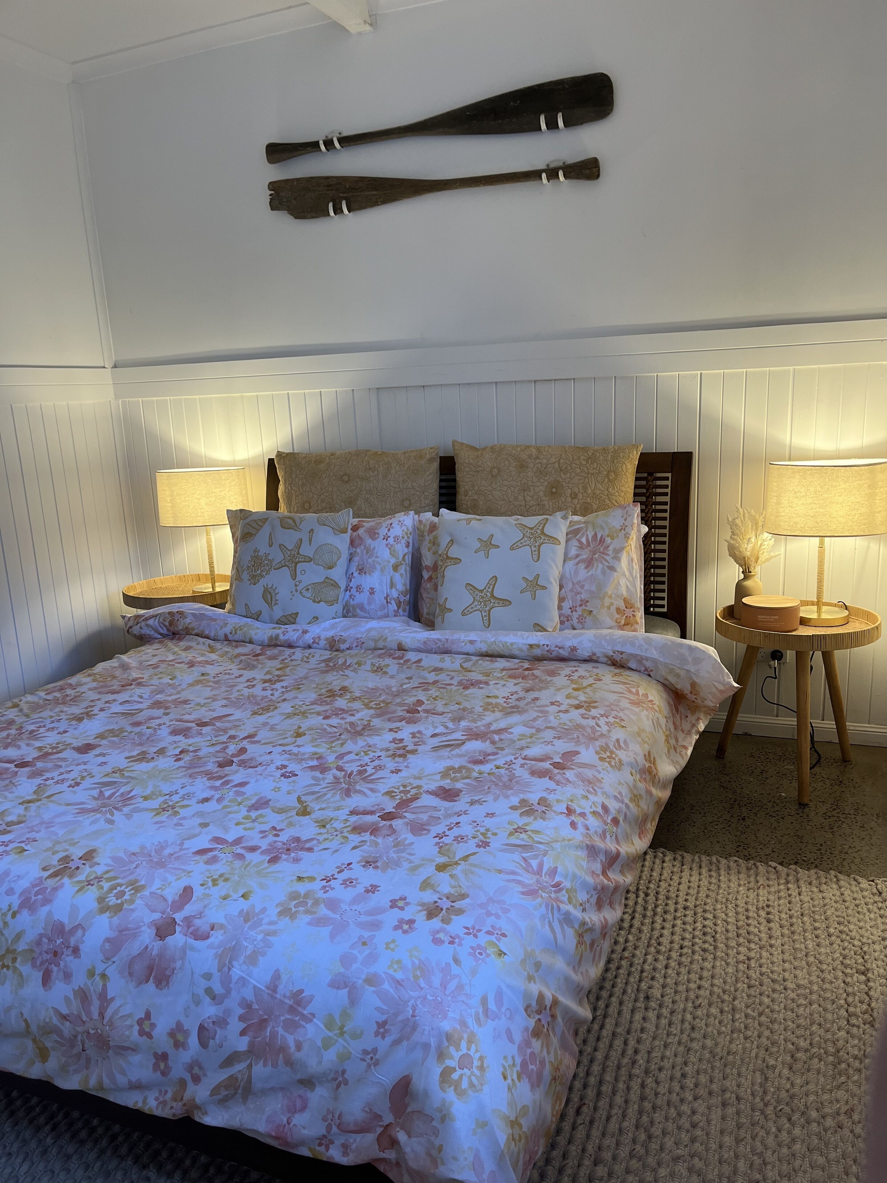 A bedroom with a floral bedspread, two bedside tables with lamps, and a wooden headboard.