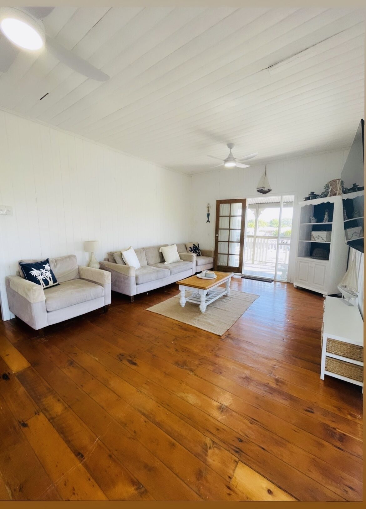 A spacious living room with wooden flooring, two sofas, a coffee table, and a ceiling fan.