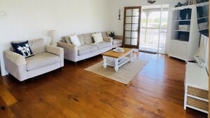 A spacious living room with wooden flooring, two sofas, a coffee table, and a ceiling fan. - Coastal Queenslander- 2 minute walk to the beach! (Woodgate)