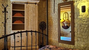 Una camera da letto rustica con un armadio in legno, un letto con copriletto floreale, una ventola a piantana e una parete in pietra.
