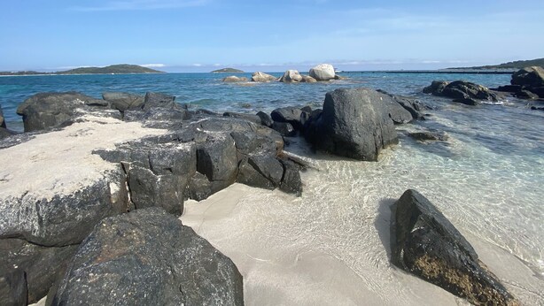 A rocky beach with clear water and distant islands.