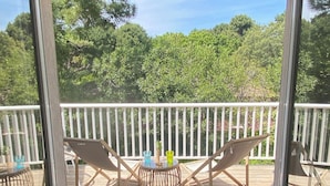 A covered outdoor deck with two lounge chairs and a small table, overlooking a forested area.