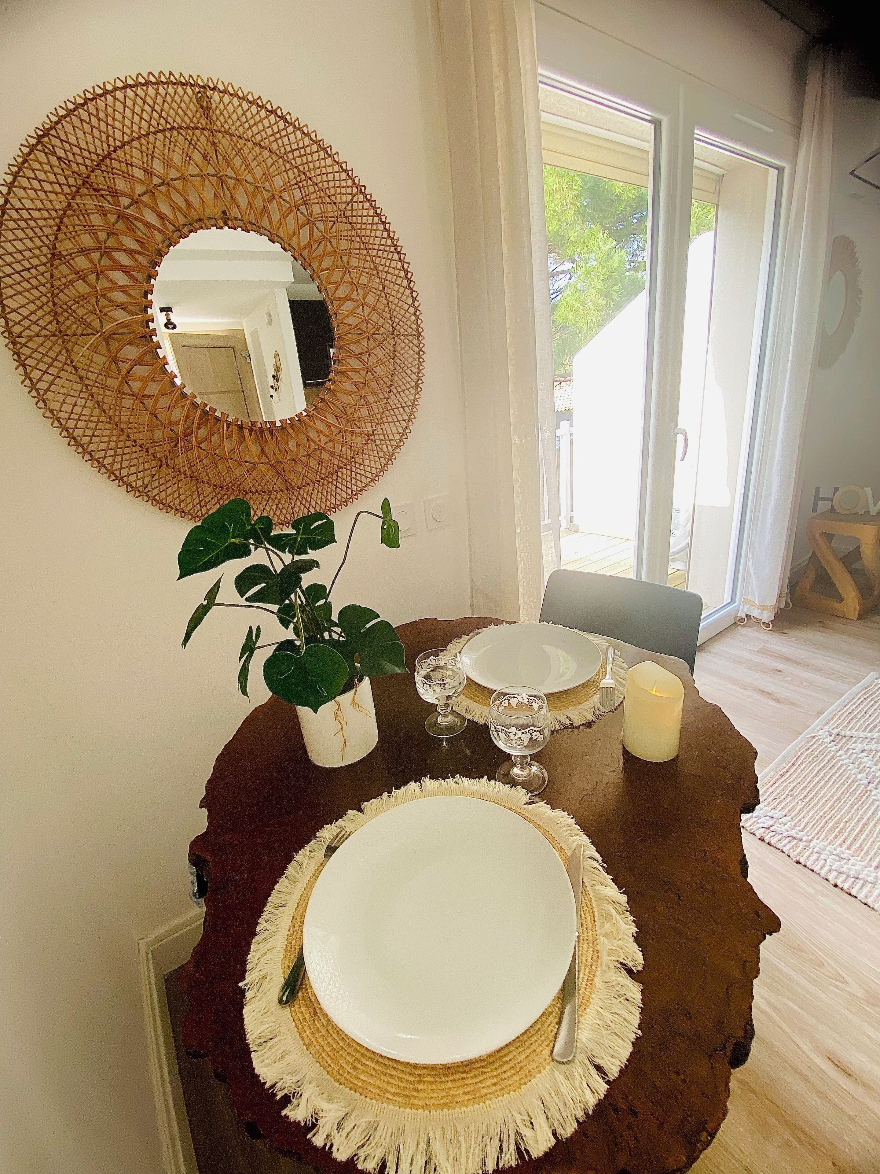 A dining area with a round table, two plates, two glasses, a candle, and a potted plant.