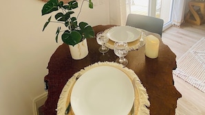 A dining area with a round table, two plates, two glasses, a candle, and a potted plant.