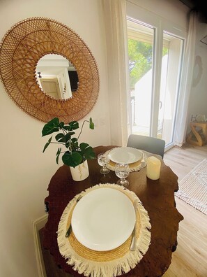 Un coin repas avec une table ronde, deux assiettes, deux verres, une bougie et une plante en pot.