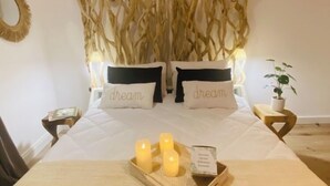 A neatly made bed with two pillows, each labeled 'dream', a bedside table with a plant, and a tray with candles and a book.