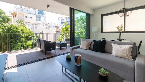 A modern living room with a grey sofa, black and white cushions, a coffee table with a plant, and a view of the city through large windows. - Charming & Quiet 1 BR in Heart Tel Aviv SAFE ROOM (Tel Aviv-Yafo)