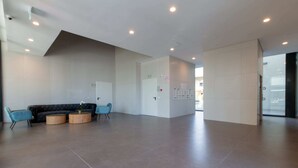 A spacious lobby with a black sofa and two round wooden tables, a white reception desk, and a glass door leading outside. - Charming & Quiet 1 BR in Heart Tel Aviv SAFE ROOM (Tel Aviv-Yafo)