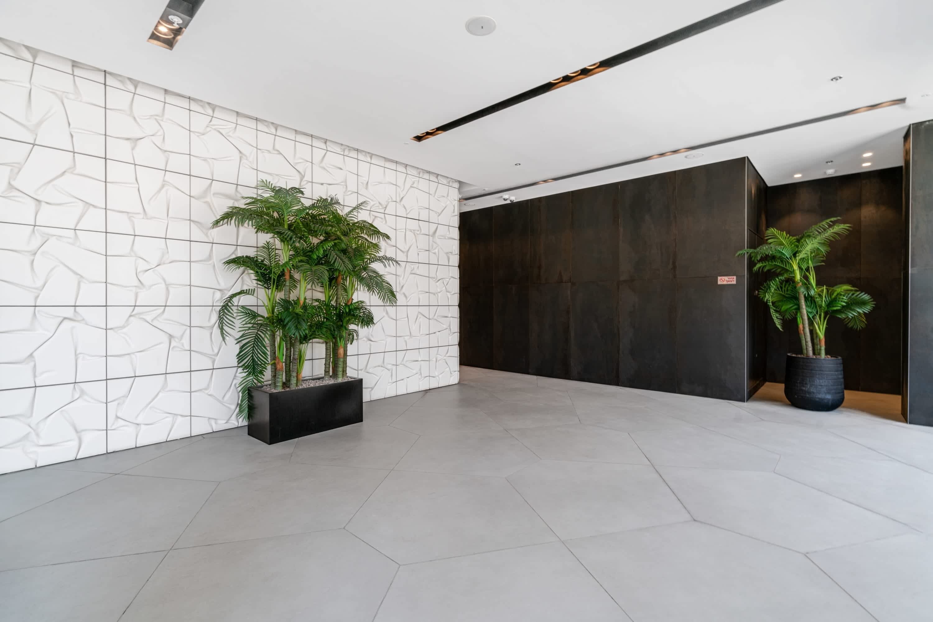 Un hall d’entrée spacieux au design moderne, avec un mur blanc à la texture particulière, un panneau en bois foncé et un sol carrelé.