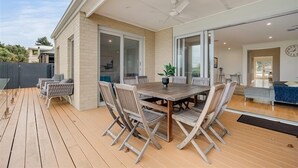 A covered patio with a wooden table and chairs, a ceiling fan, and a view of the interior through glass doors.