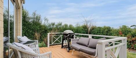 A wooden deck with outdoor furniture, including a sofa and chairs, and a grill.