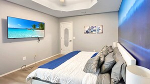 Een slaapkamer met een bed, een televisie, een deur en een muur met een schilderij.