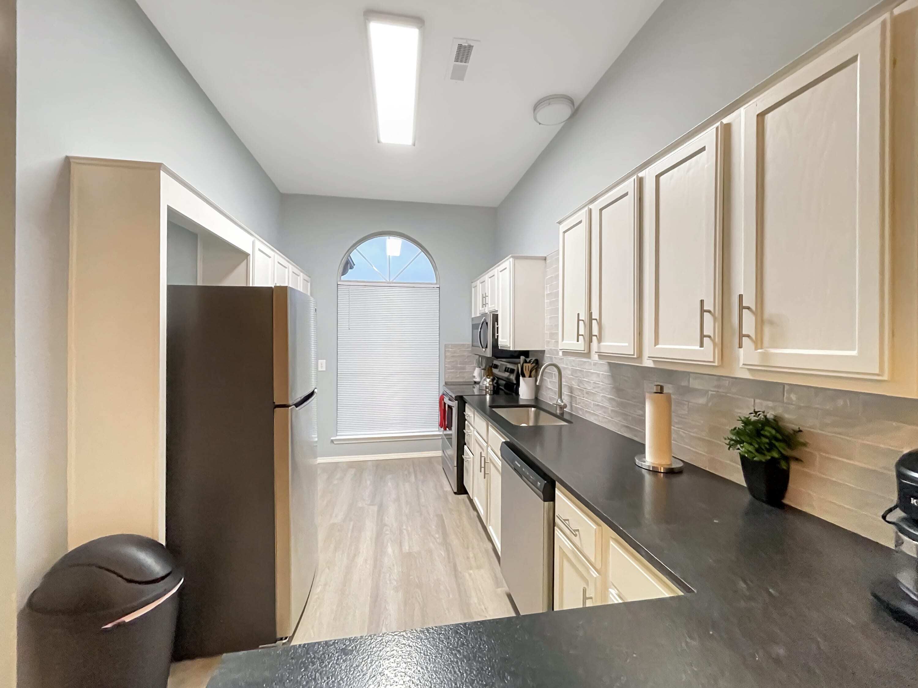 A modern kitchen with light-colored cabinets, a black countertop, and a built-in dishwasher.