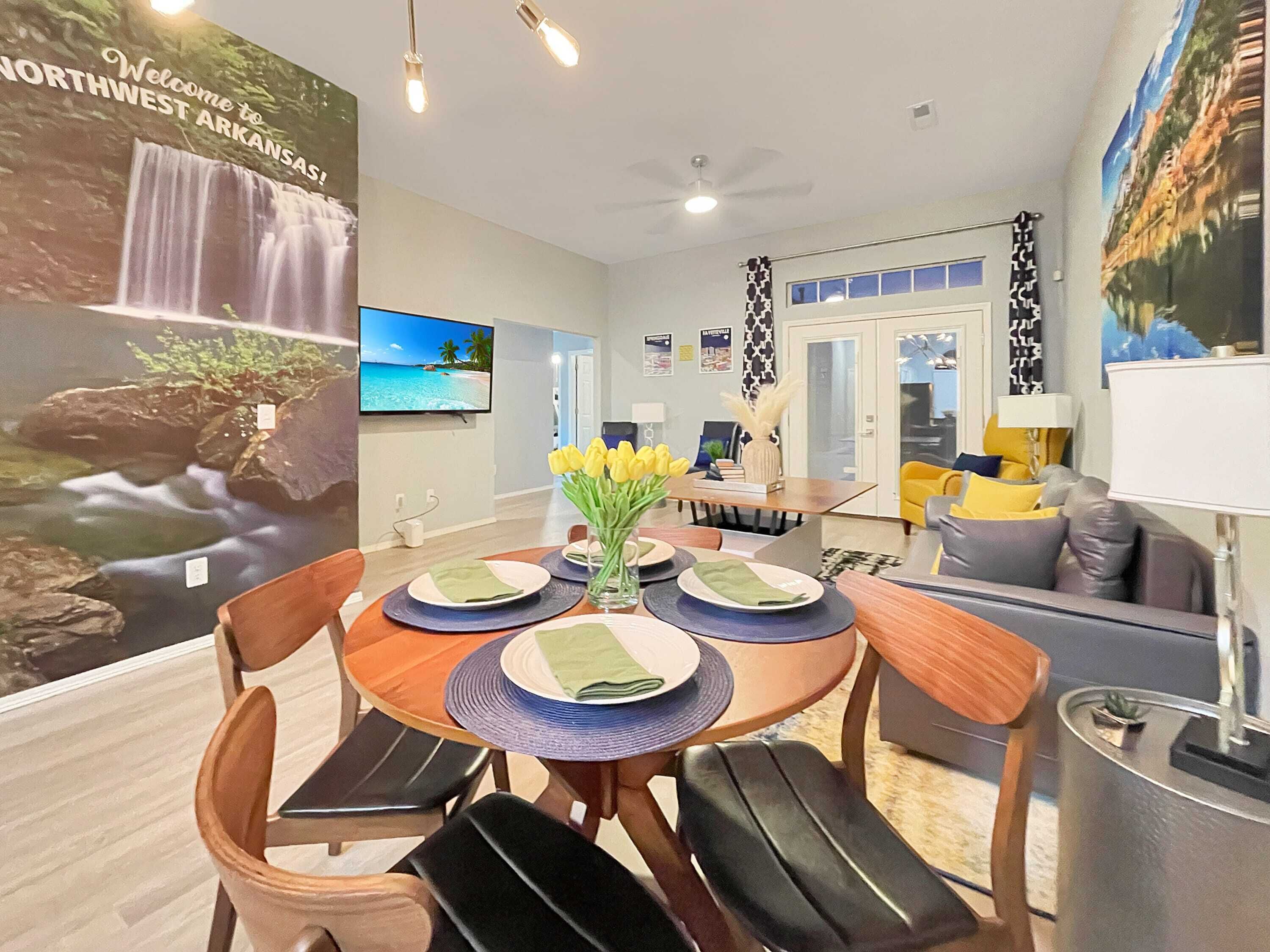 A dining area with a table set for four, a TV mounted on the wall, and a view of a waterfall on the poster.
