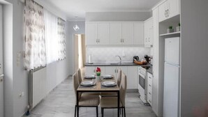 A modern kitchen with white cabinets, a dining table set for two, and a refrigerator. - Detatched house - 1km from the beach. (KOS STATE - DODECANESE)
