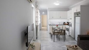 A modern kitchen with white cabinets, a dining table with chairs, and a small island with a sink. - Detatched house - 1km from the beach. (KOS STATE - DODECANESE)