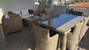 Un balcón con mobiliario de mimbre, incluyendo un sofá y una mesa, con vistas a una zona residencial.