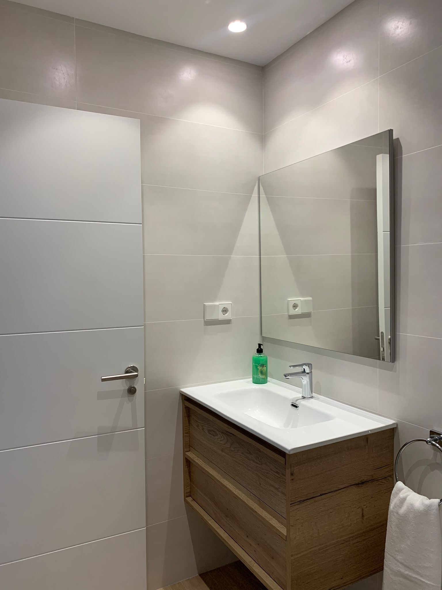 Un baño moderno con lavamanos blanco, tocador de madera y un espejo grande.