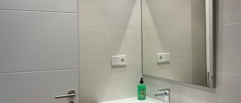 Un baño moderno con lavamanos blanco, tocador de madera y un espejo grande.