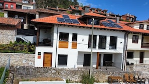 Un edificio a due piani con tetto in tegole rosse, pannelli solari e fondamenta in muratura.