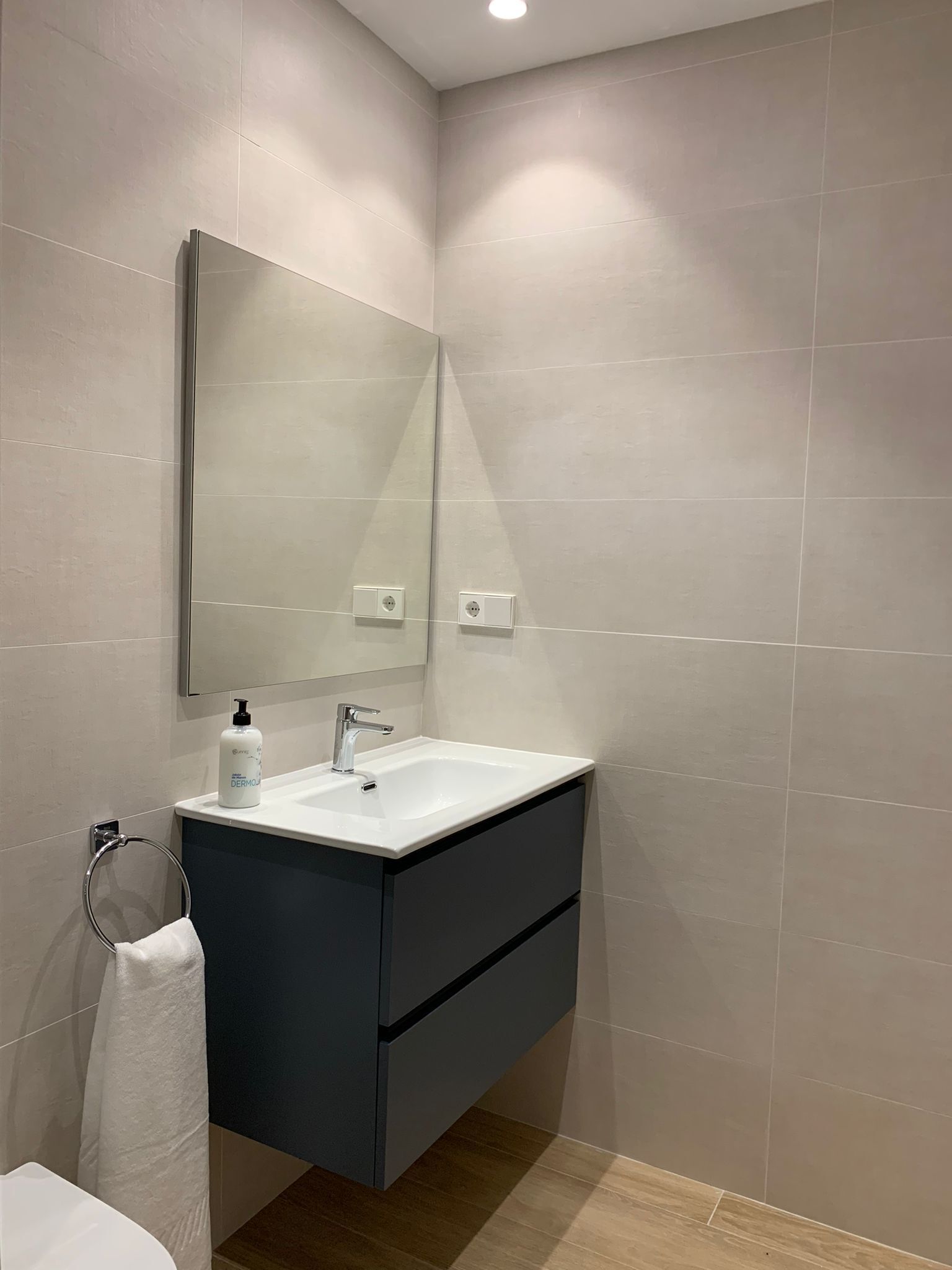 Une salle de bain moderne avec un grand miroir, un lavabo blanc et un meuble-lavabo foncé.