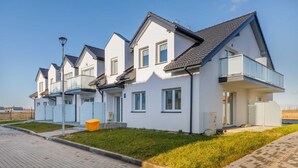 Una hilera de casas modernas, de color blanco con techos grises, cada una con un balcón y un pequeño jardín delantero.