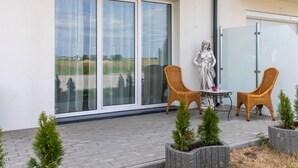 Un balcón con dos sillones de mimbre, una estatua y vista del paisaje a través de puertas de vidrio grandes.